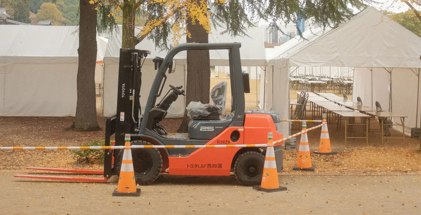 Orange forklift behind traffic cones next to white event tents