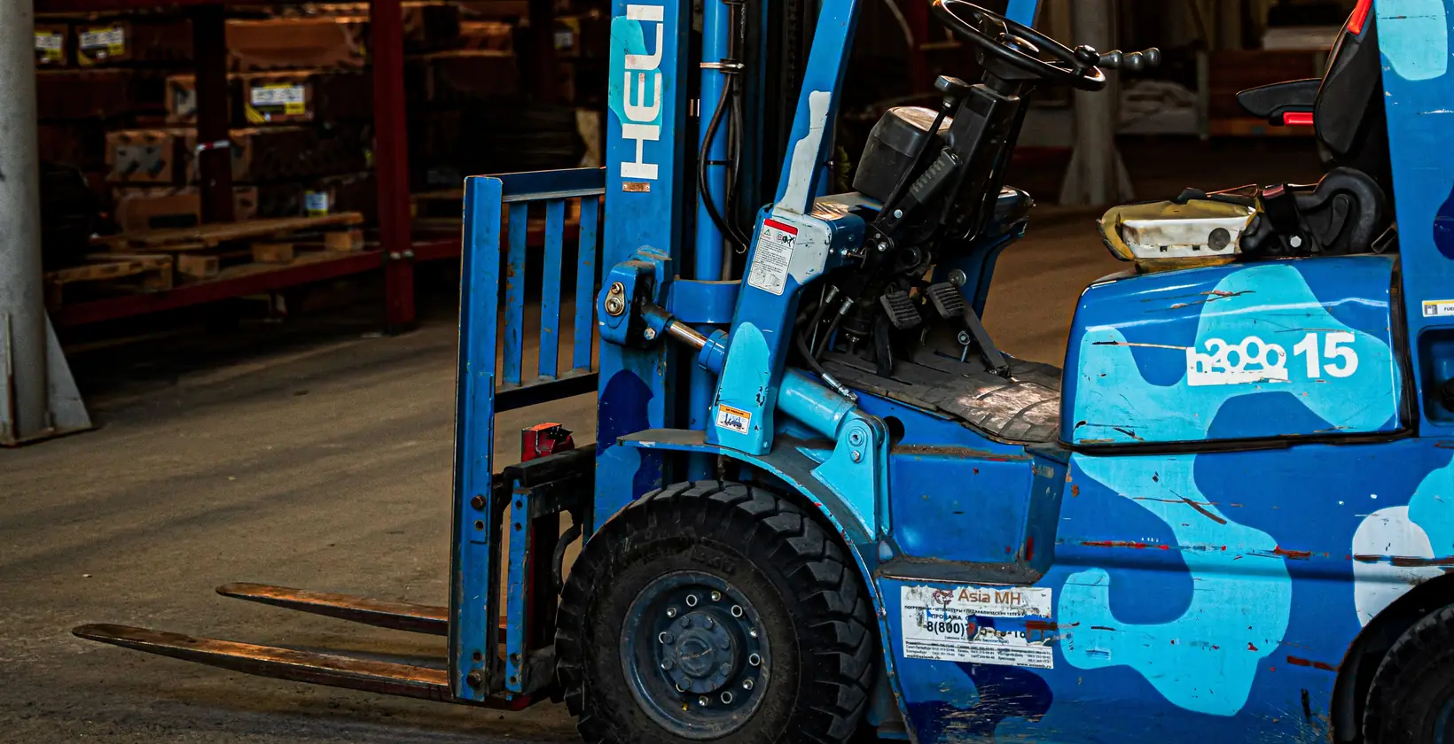 Blue forklift with camouflage paint parked inside a sunlit warehouse