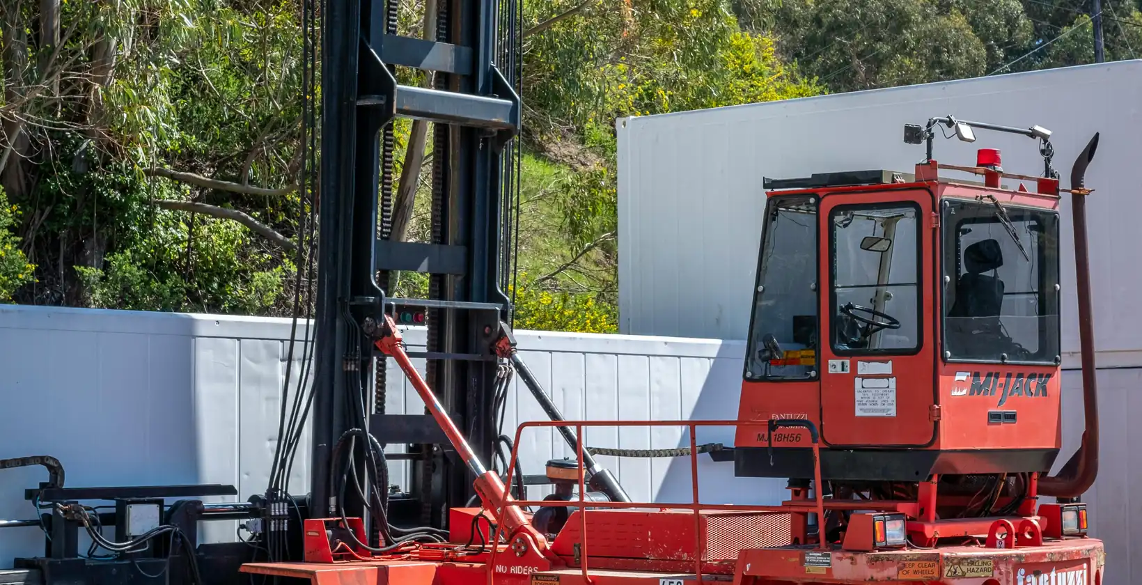 Red container handler with a tall mast parked in an outdoor yard